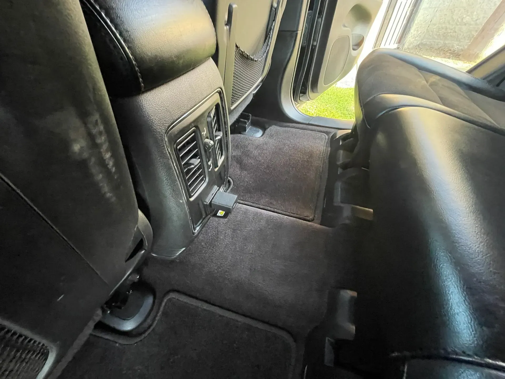 Rear interior of a vehicle featuring black leather seats, a center console with air vents, and carpeted floor mats.