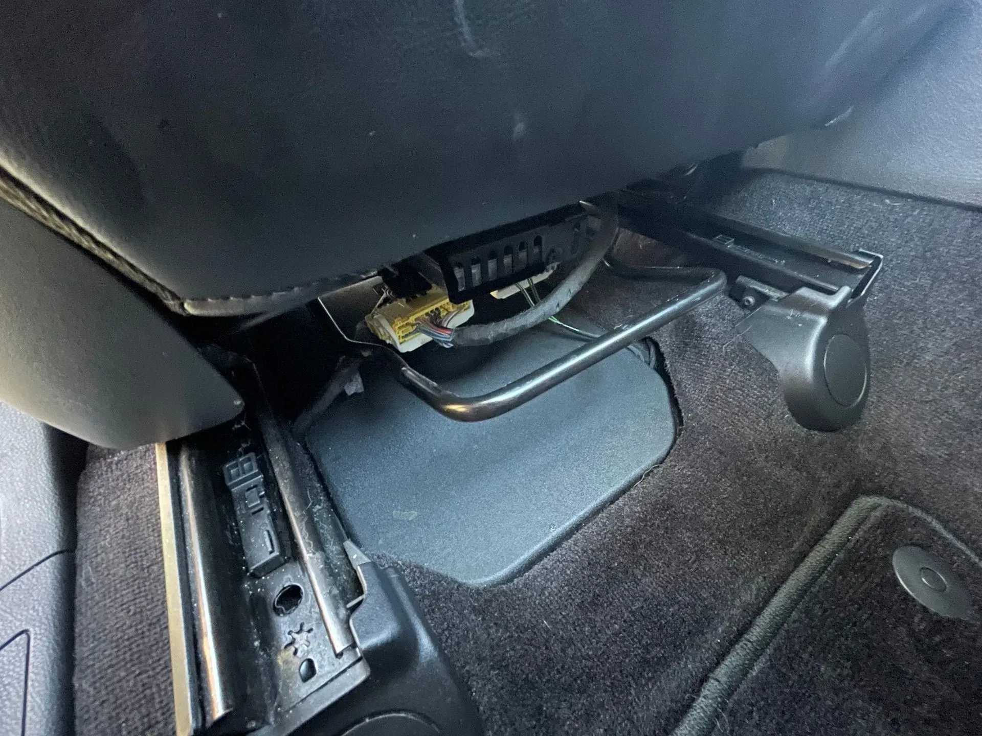 Under-seat view of a car interior showing seat rails, a seat adjustment lever, and yellow electrical wiring connectors.