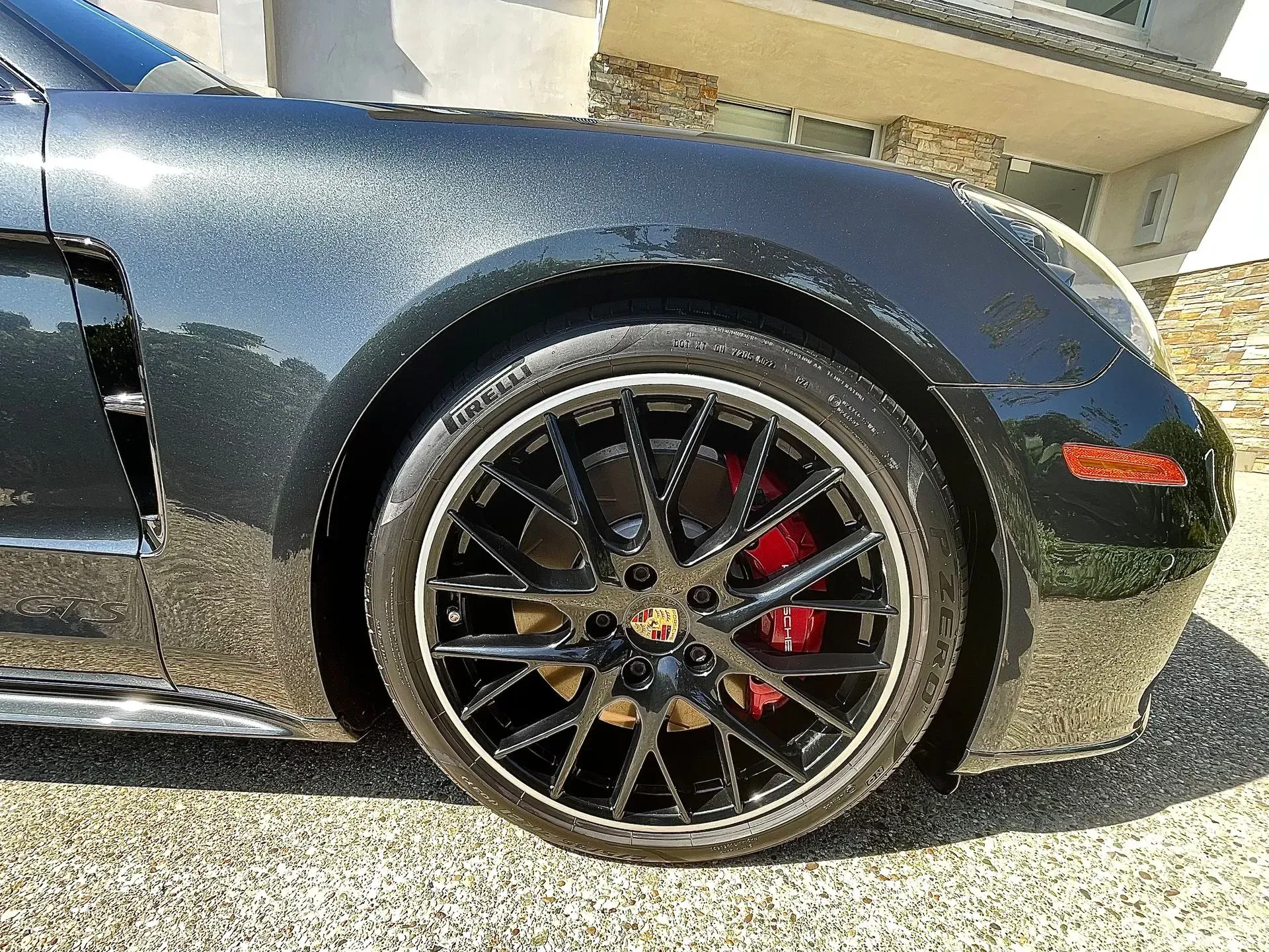 Close-up of a dark grey Porsche front wheel with black multi-spoke rims and a visible red brake caliper.