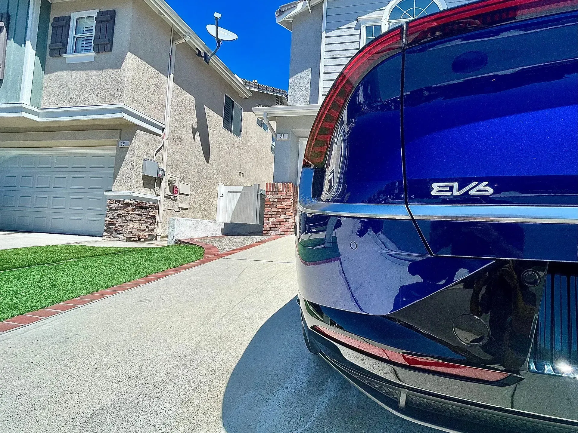 A close-up view of the rear of a dark blue Kia EV6 parked in a residential driveway near a house.