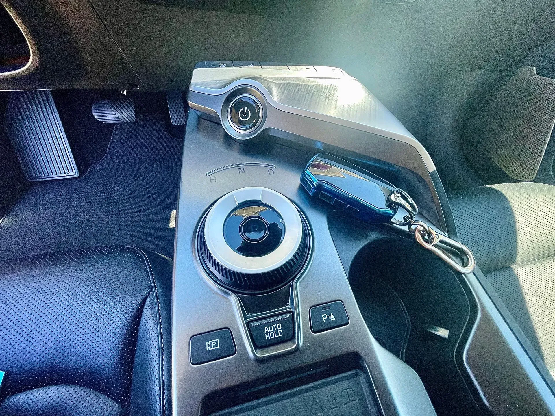 A car center console featuring a rotary gear selector, parking buttons, a start button, and a key fob.
