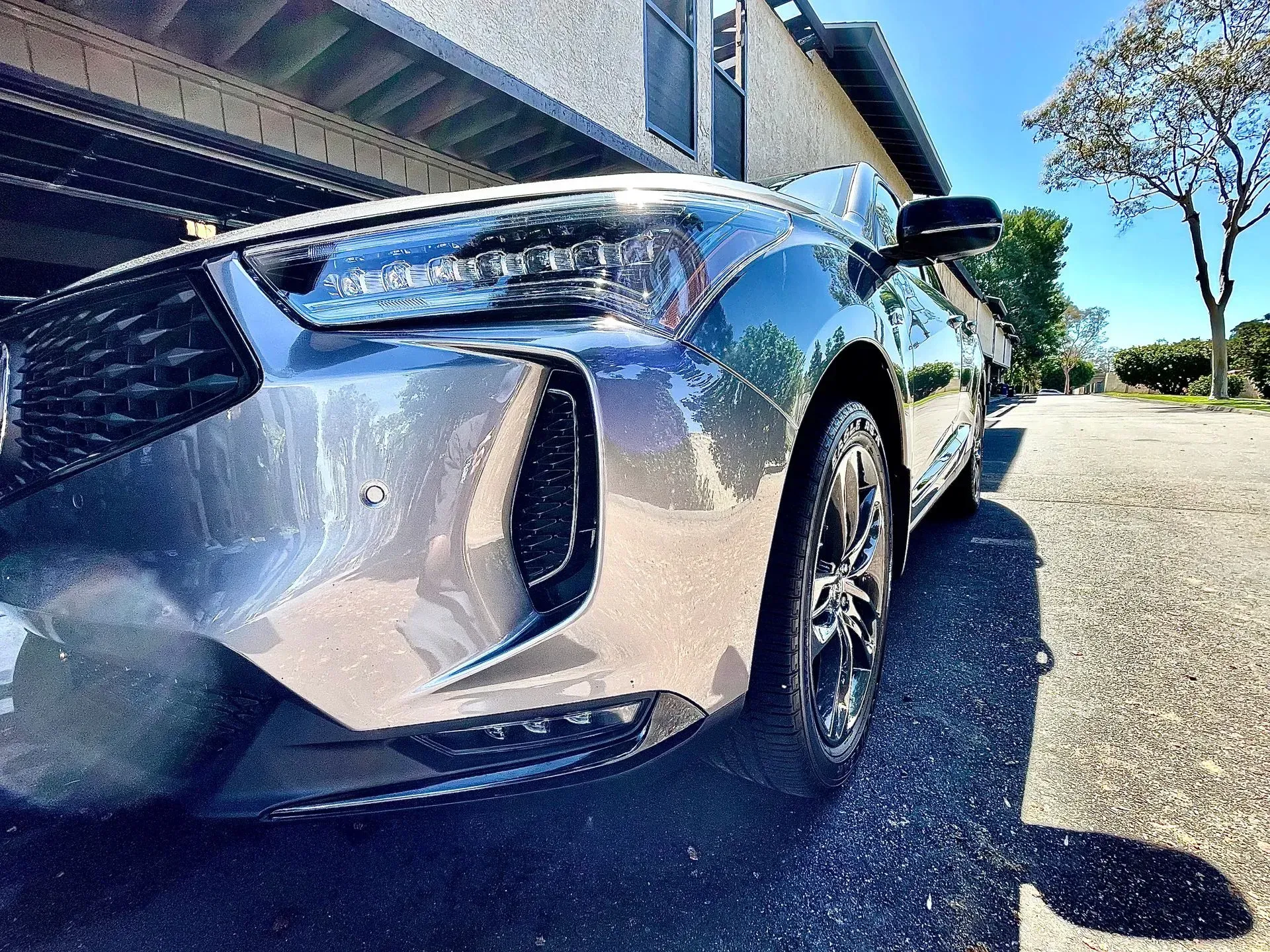 A low-angle view of the front passenger side of a dark gray sedan parked on a gravel path near a building.
