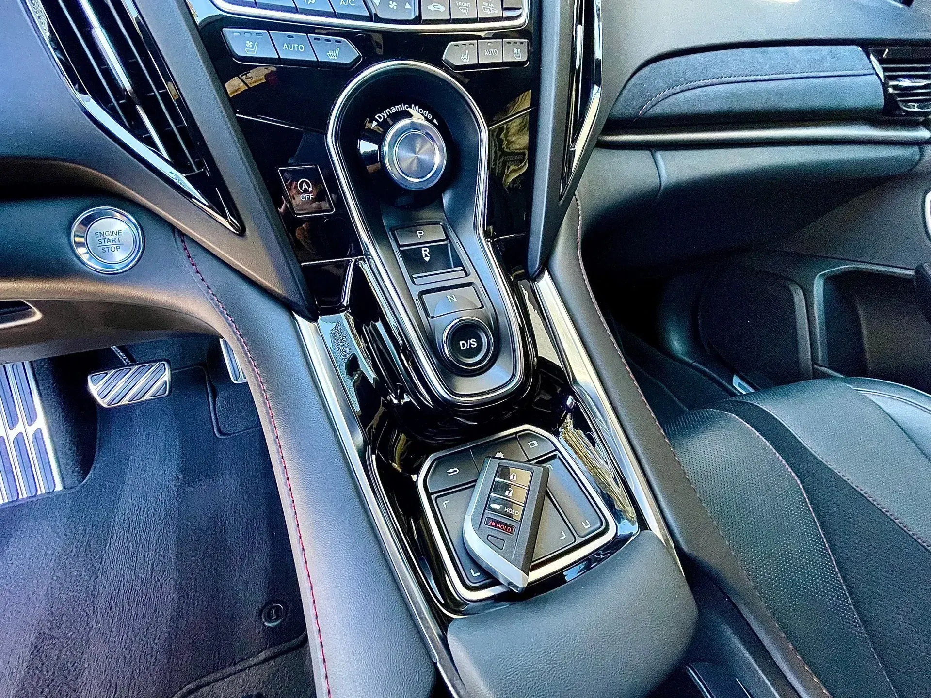 A high-angle view of a luxury vehicle's center console featuring a prominent rotary gear shifter and a car key fob.
