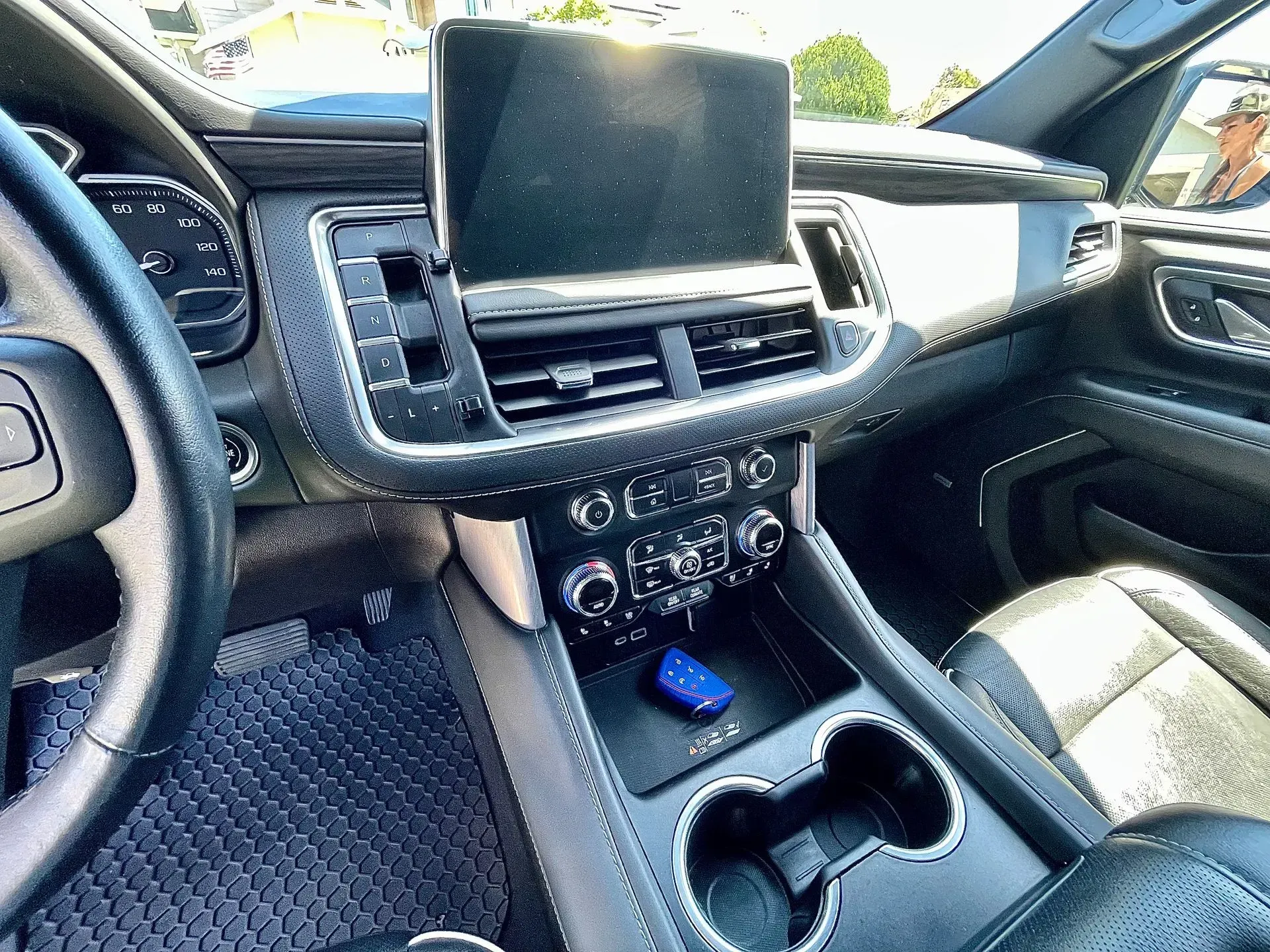 The interior of a vehicle dashboard featuring a central infotainment screen, air vents, control knobs, and cup holders.