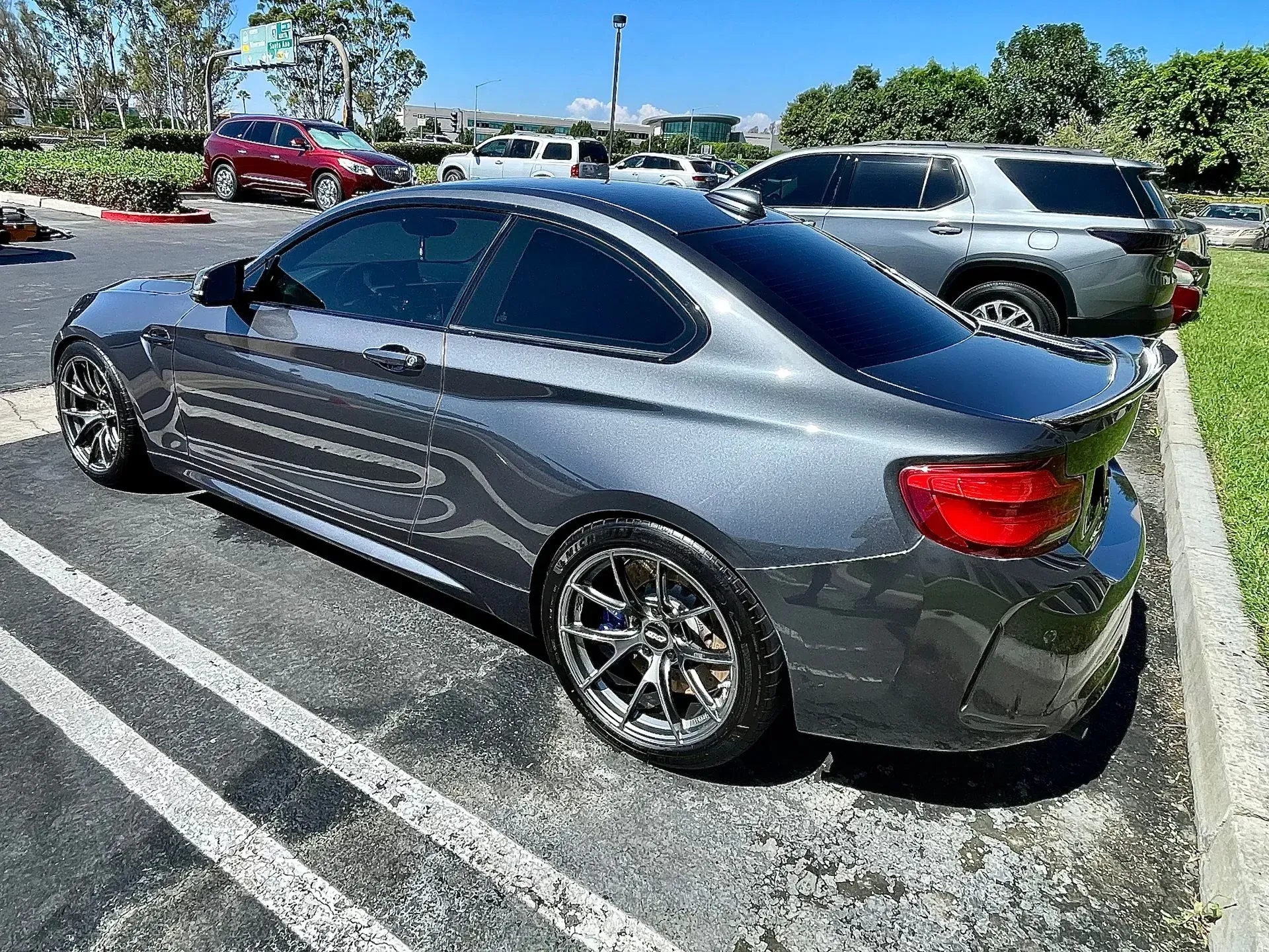 A grey BMW coupe parked in an outdoor lot on a sunny day, viewed from the rear passenger side.