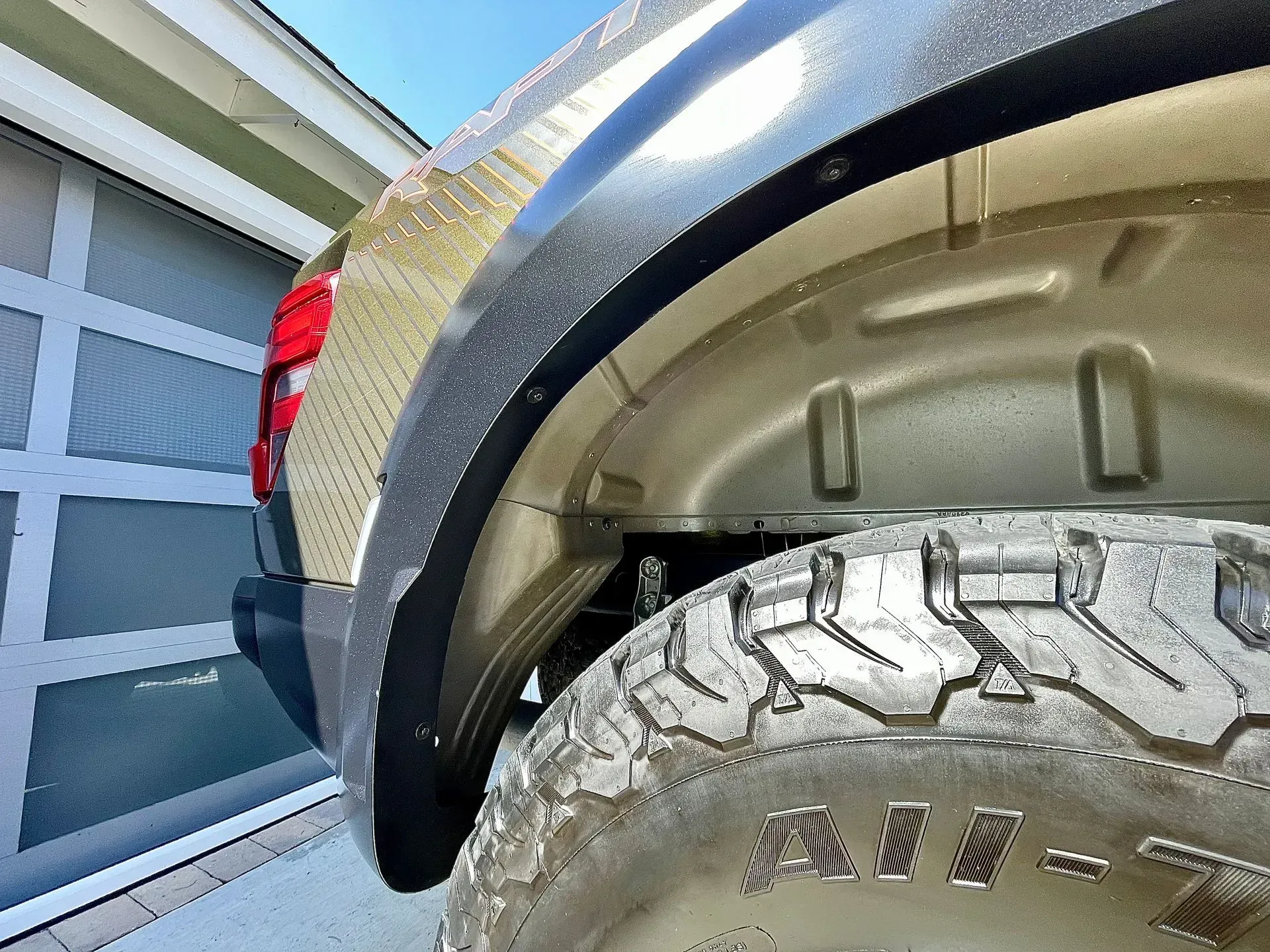 Close-up of a truck's rear wheel well, featuring a black fender flare, knobby tire, and light-colored body paint.