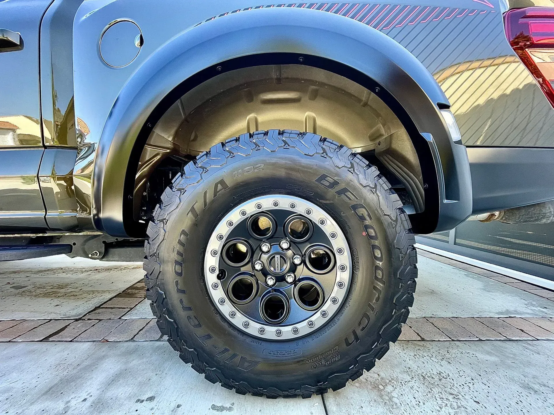 A close-up of a black truck's rear wheel with a rugged, all-terrain tire and a custom black and silver rim.