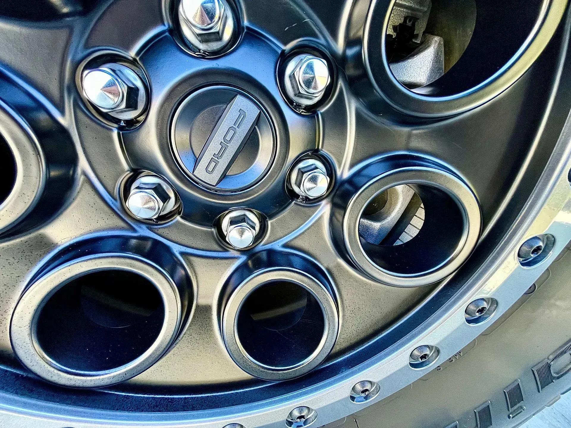 A close-up view of a matte black vehicle wheel with a circular center cap and decorative chrome lug nuts.
