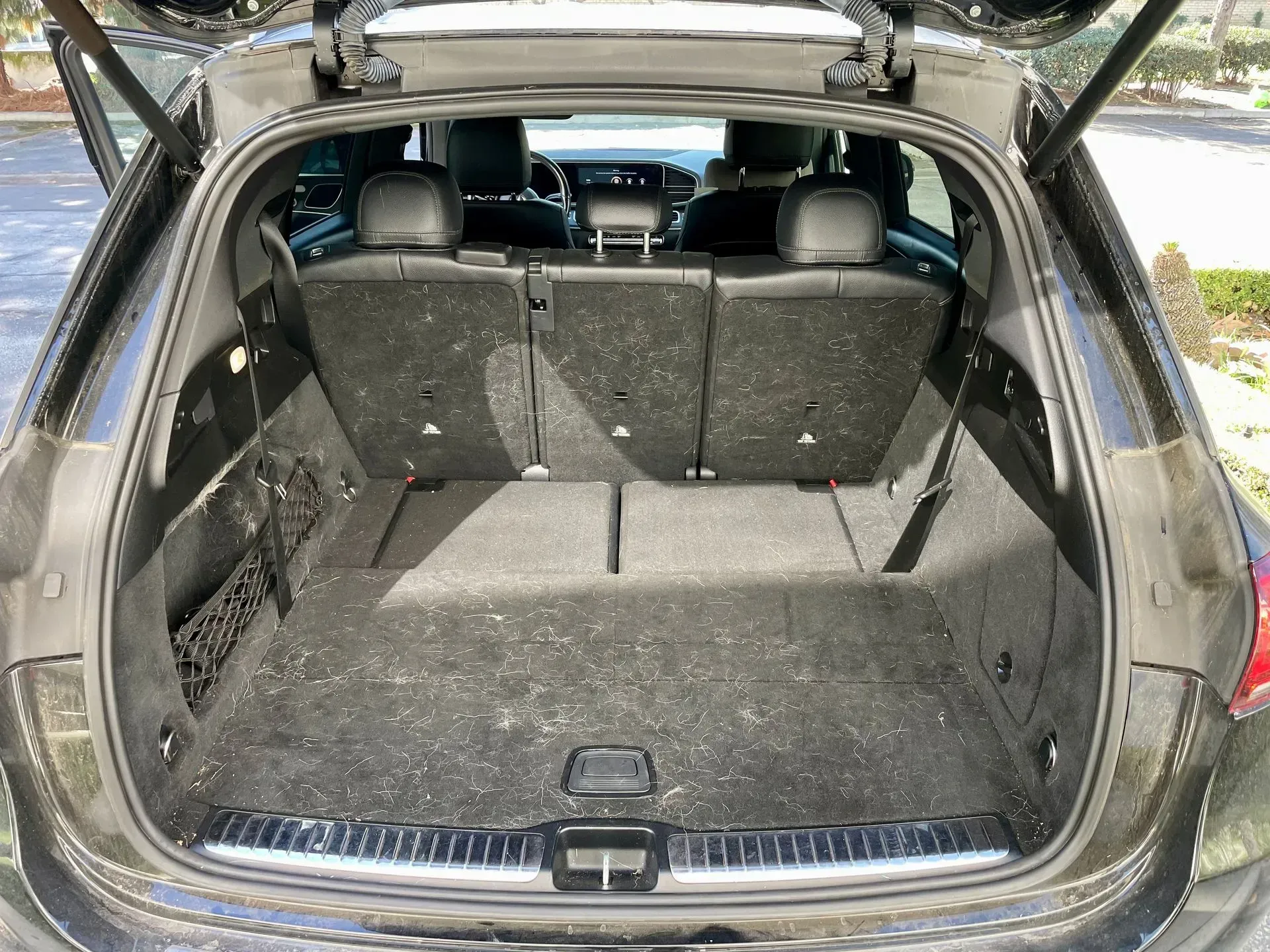 The trunk of a dark vehicle with its rear seats upright, showcasing the carpeted cargo area and storage space.