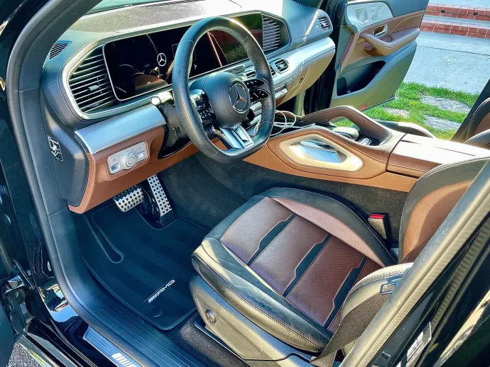 The front interior of a luxury vehicle features a leather steering wheel and two-tone brown and black upholstered seats.