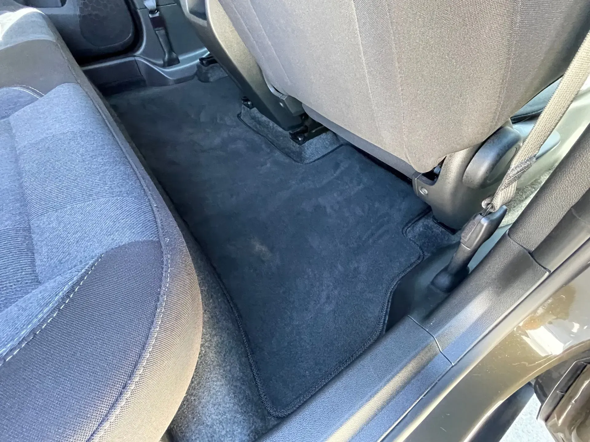 Interior view of a vehicle's back seat, showing dark blue fabric upholstery and a clean, carpeted floor mat.