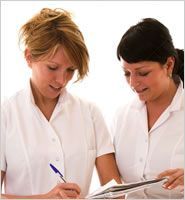 Two practitioners are looking at a clipboard and writing on it.