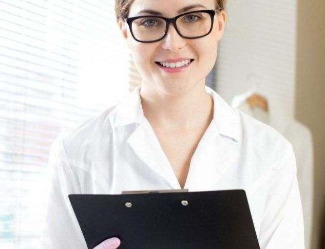 A woman wearing glasses is holding a clipboard and smiling.