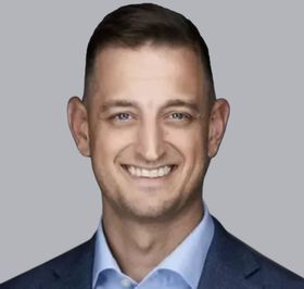 Smiling man in a blue suit and light blue shirt against a gray background.
