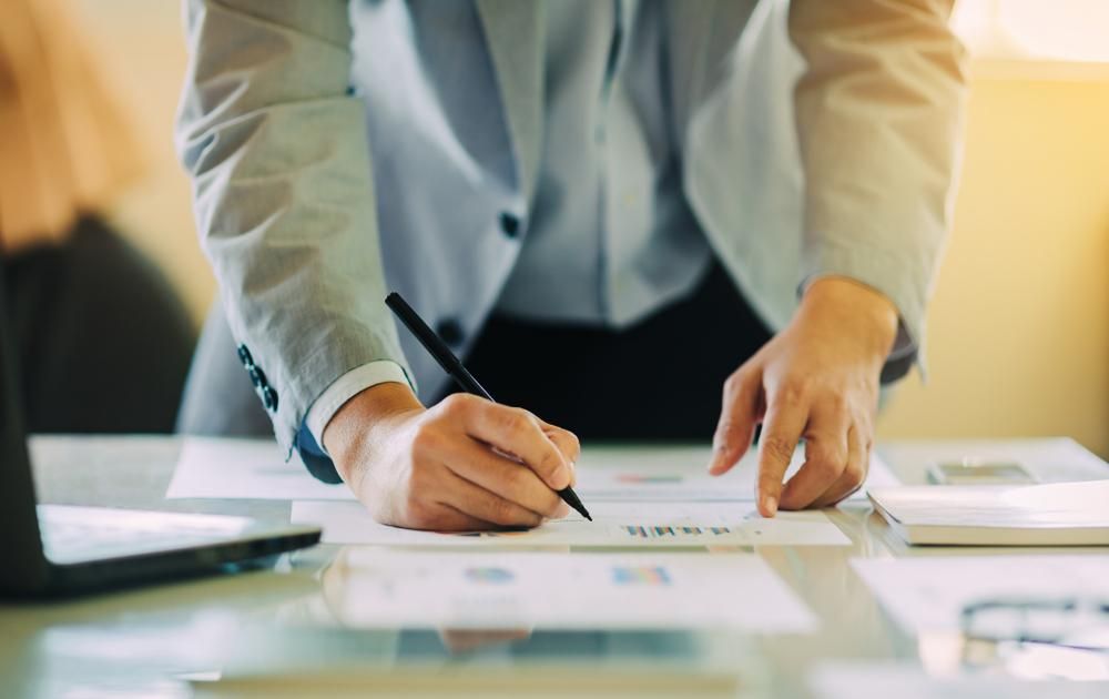 A Man Is Standing At A Desk Writing On A Piece Of Paper — Saracens Financial Consultants In Alstonville, NSW