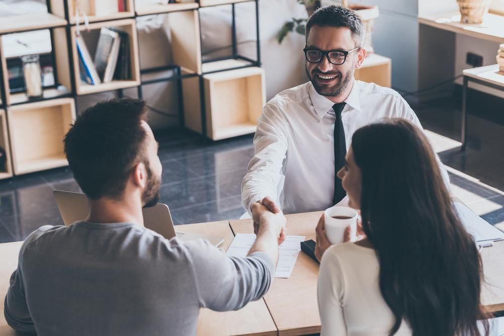 A Man Is Shaking Hands With A Woman And A Man While Sitting At A Table — Saracens Financial Consultants In Alstonville, NSW