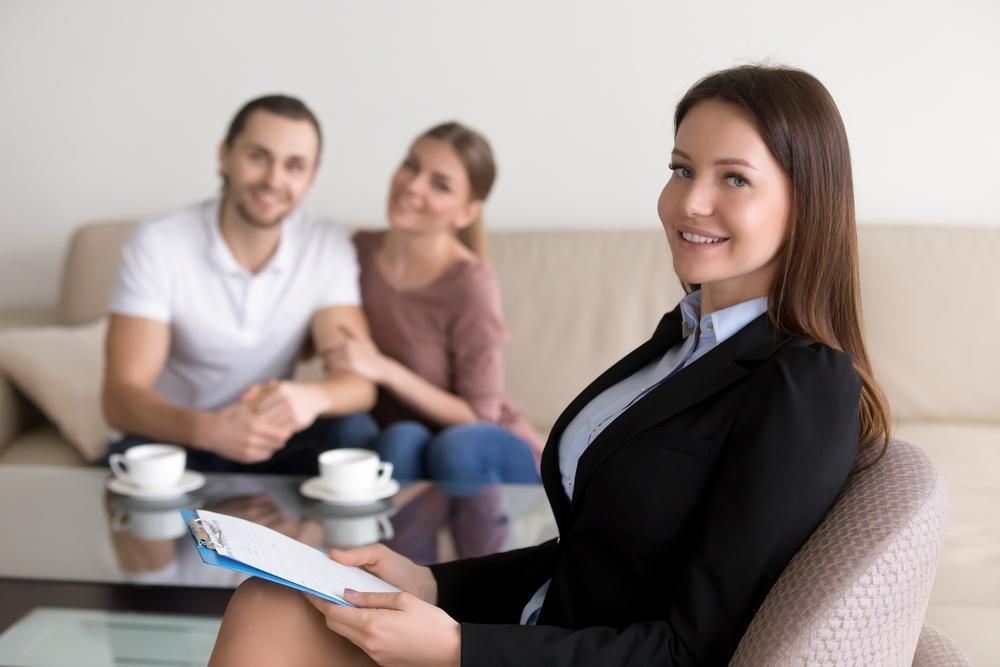 A Woman Is Sitting In A Chair With A Clipboard In Front Of A Couple — Saracens Financial Consultants In Alstonville, NSW