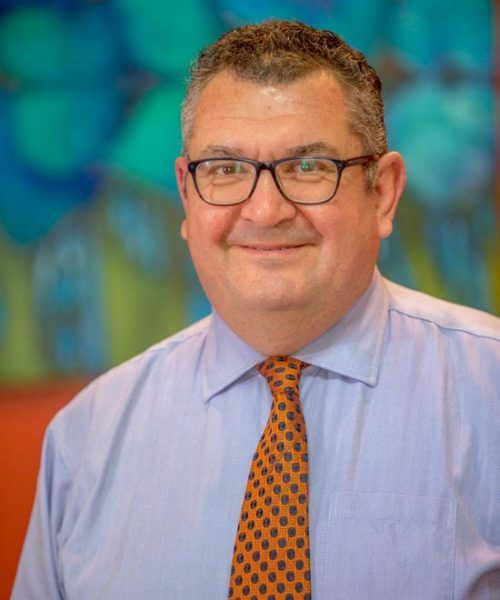 A Man Wearing Glasses And An Orange Tie Is Smiling For The Camera — Saracens Financial Consultants In Alstonville, NSW