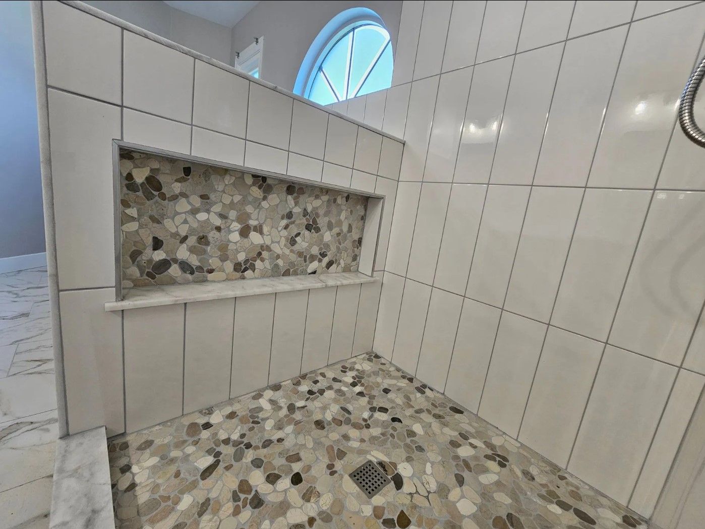 Shower with white tiled walls, pebble floor, and built-in niche with stone mosaic.