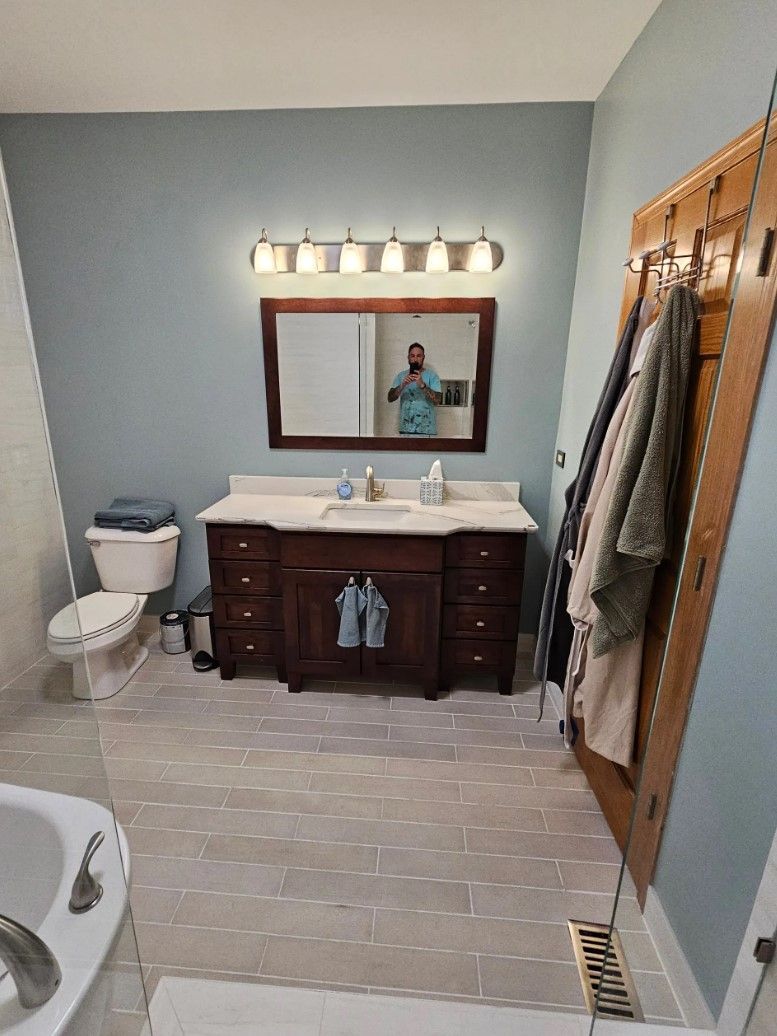 Bathroom with a vanity, mirror, and a towel rack. Pale blue walls, dark wood cabinetry, and grey tiled floor.