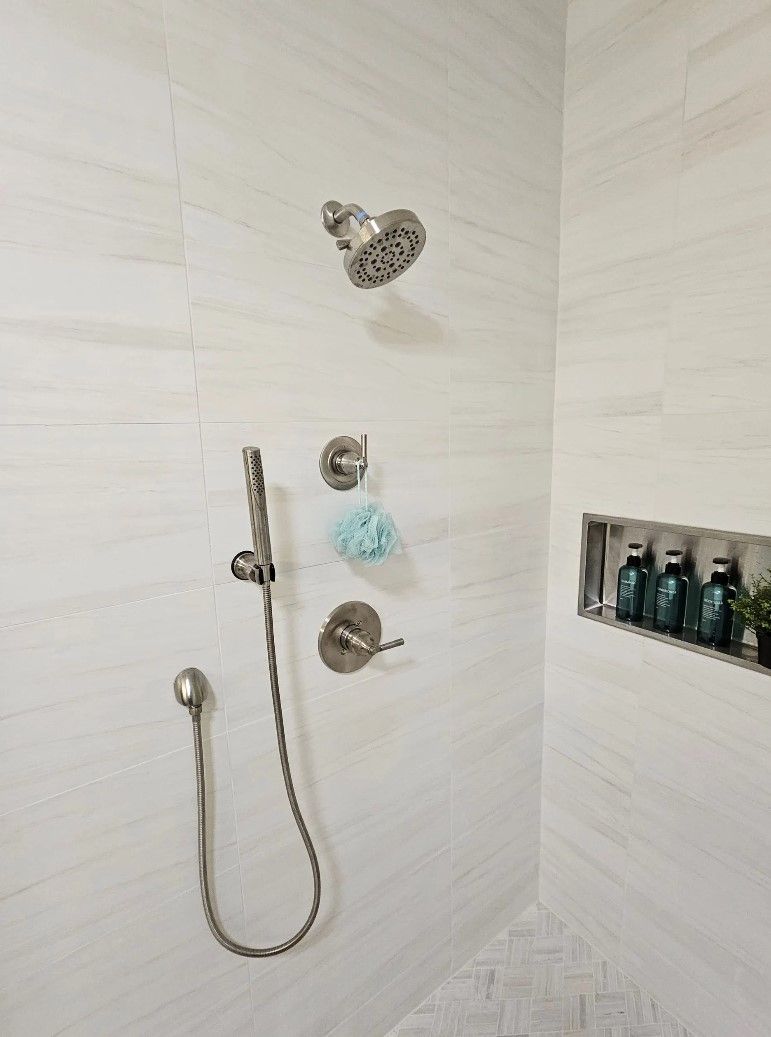 Shower with white tiled walls, silver fixtures, and a built-in shelf holding toiletries.