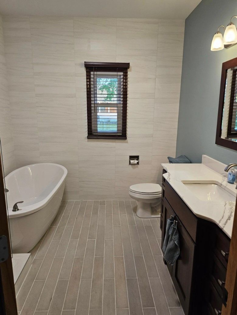Bathroom with tub, toilet, vanity, window with dark wood trim, light tile.