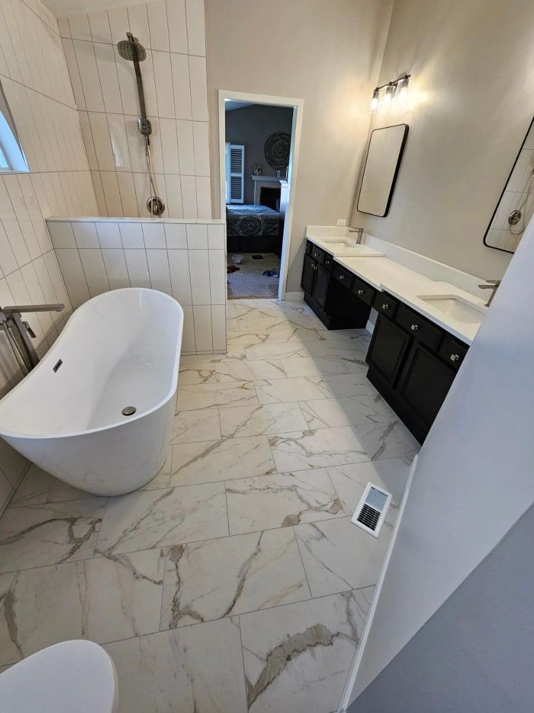 Bathroom with white tub, marble floor, double vanity, and doorway to bedroom.
