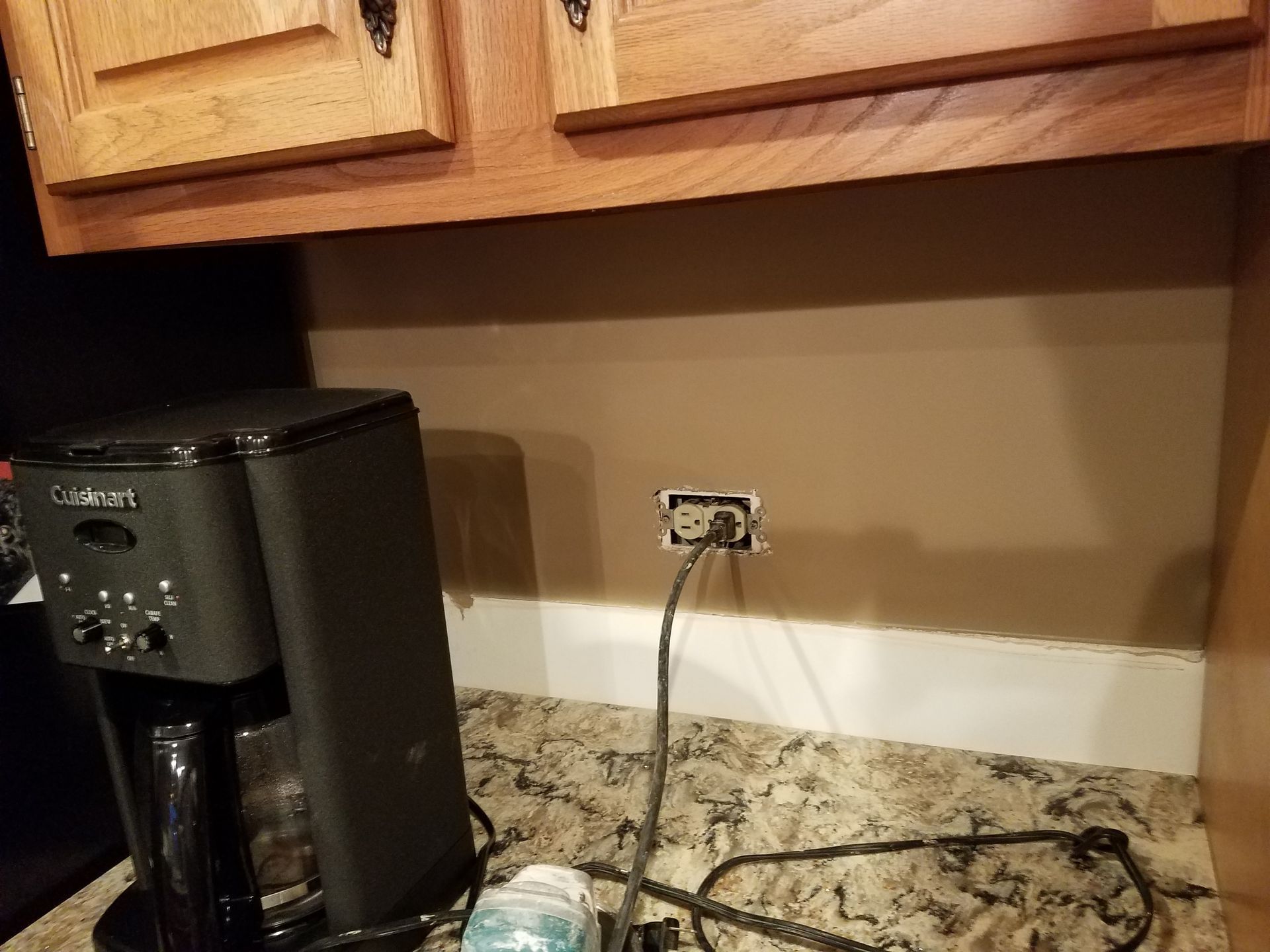 Coffee maker plugged into outlet on tan kitchen wall.