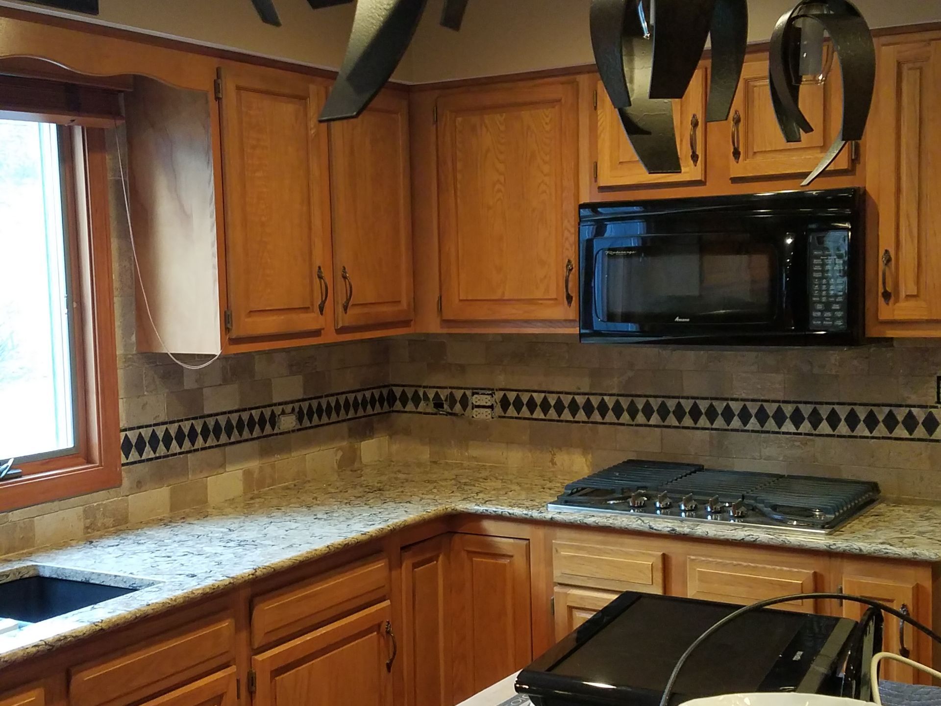 Kitchen with light brown cabinets, granite countertops, black microwave, and stove.