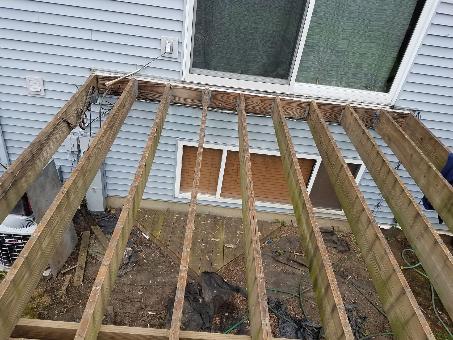 Decayed deck structure with exposed joists; partially removed deck boards; near a house.