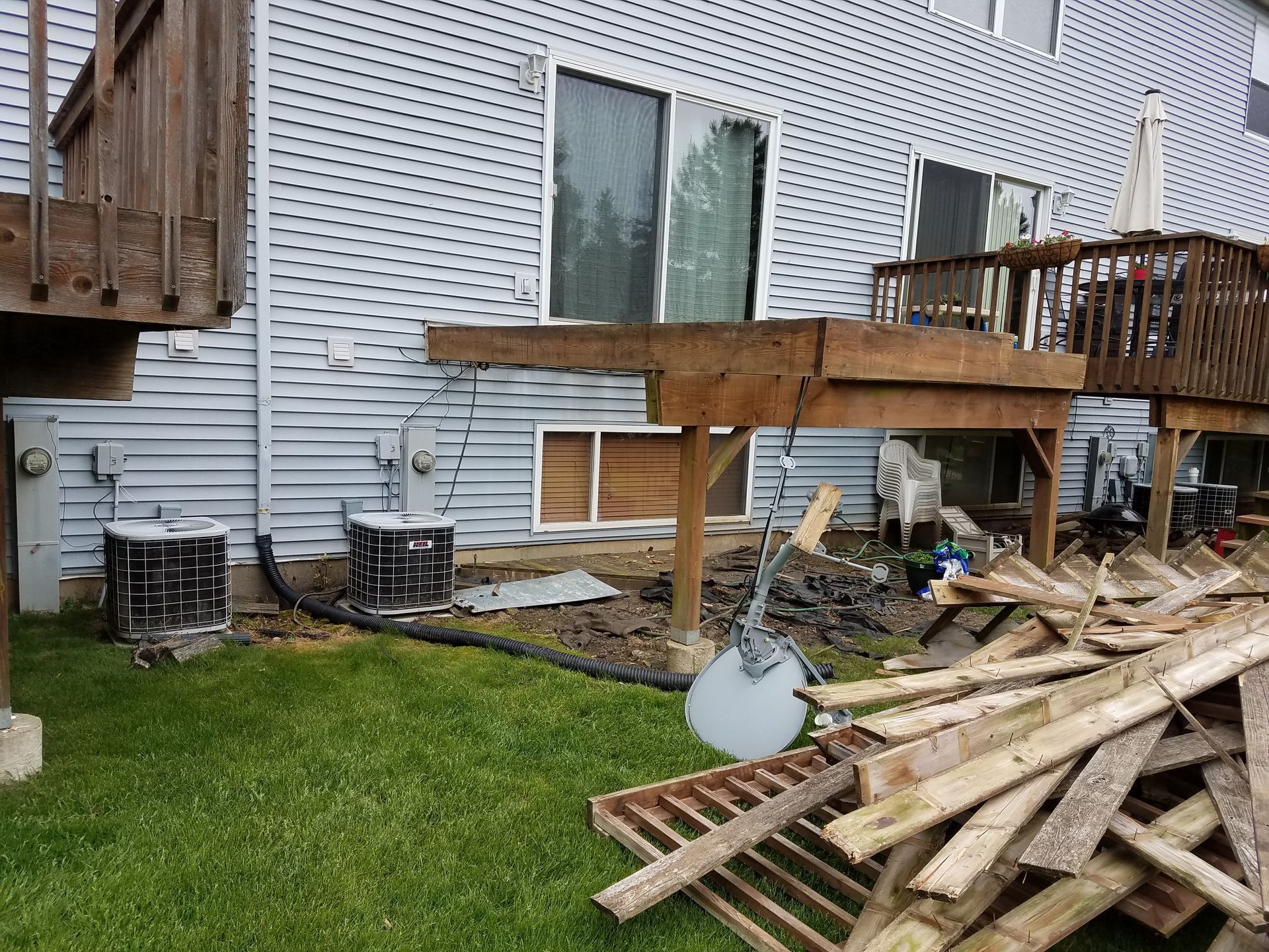 Backyard with two decks, AC units, and wood debris. The siding is light gray, and the grass is green.