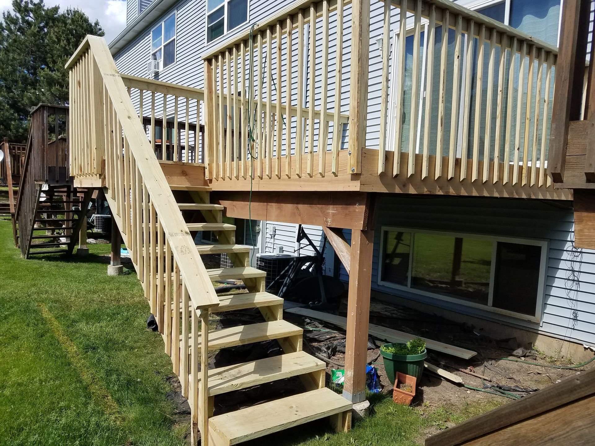 Wooden deck with stairs attached to a house, on a grassy lawn.