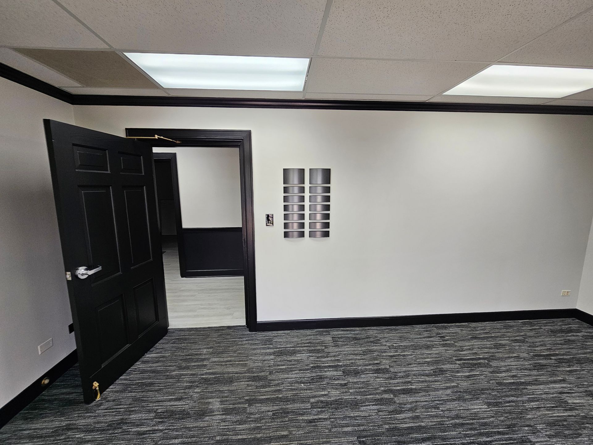 Black door ajar in empty office. White walls with black trim and carpeted floor.