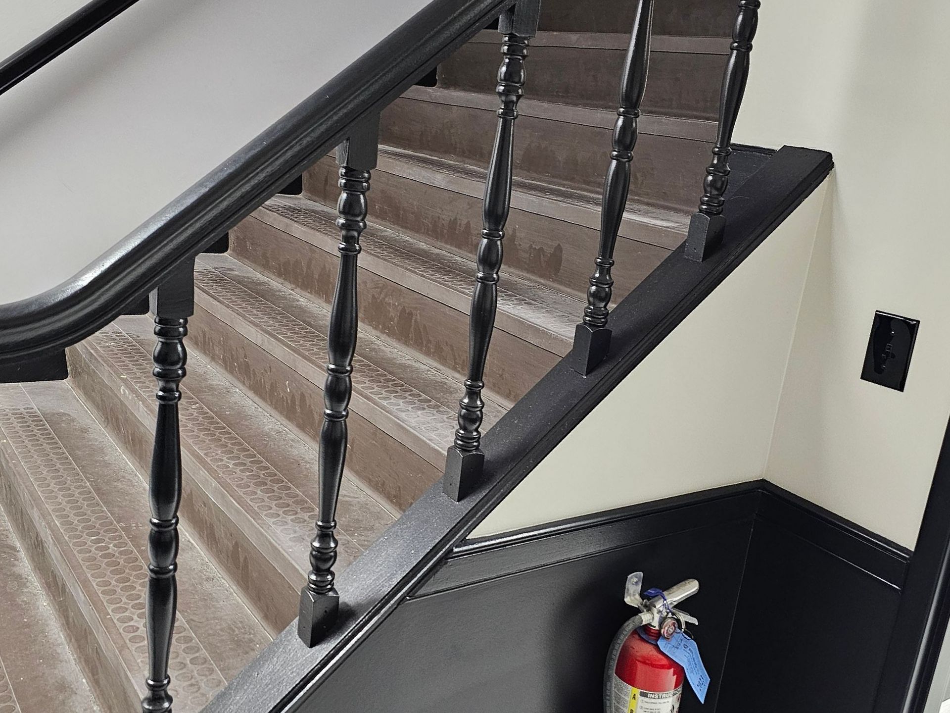 Staircase with black banister, carpeted stairs, and fire extinguisher.