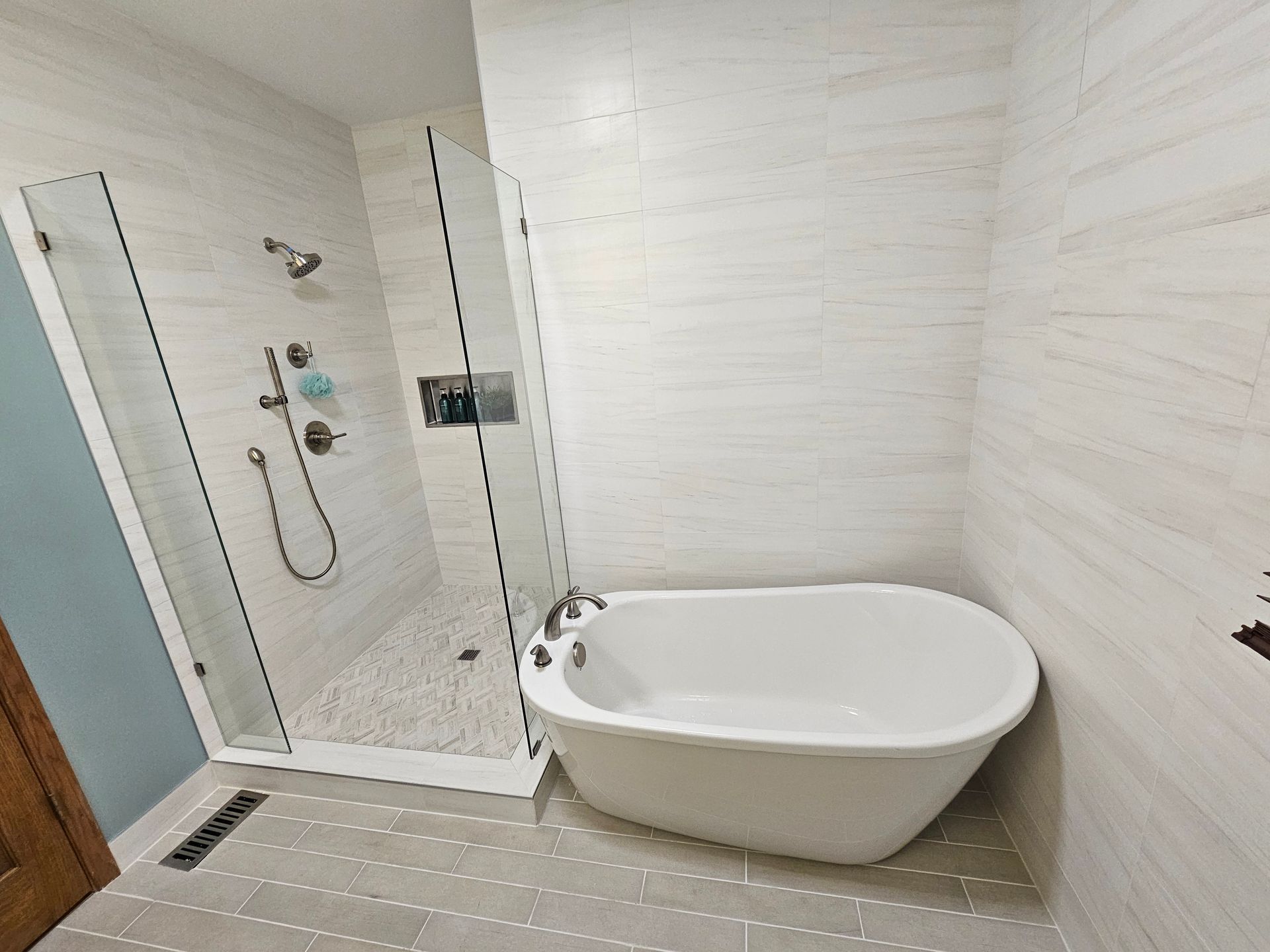 Bathroom with a white tub, glass shower, and light-colored tiled walls and floor.