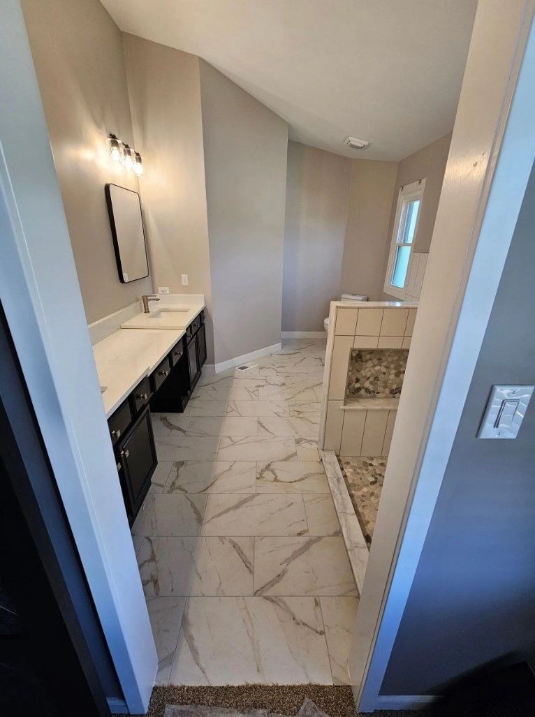 Bathroom with marble tile floor, black vanity, and a walk-in shower with glass doors.