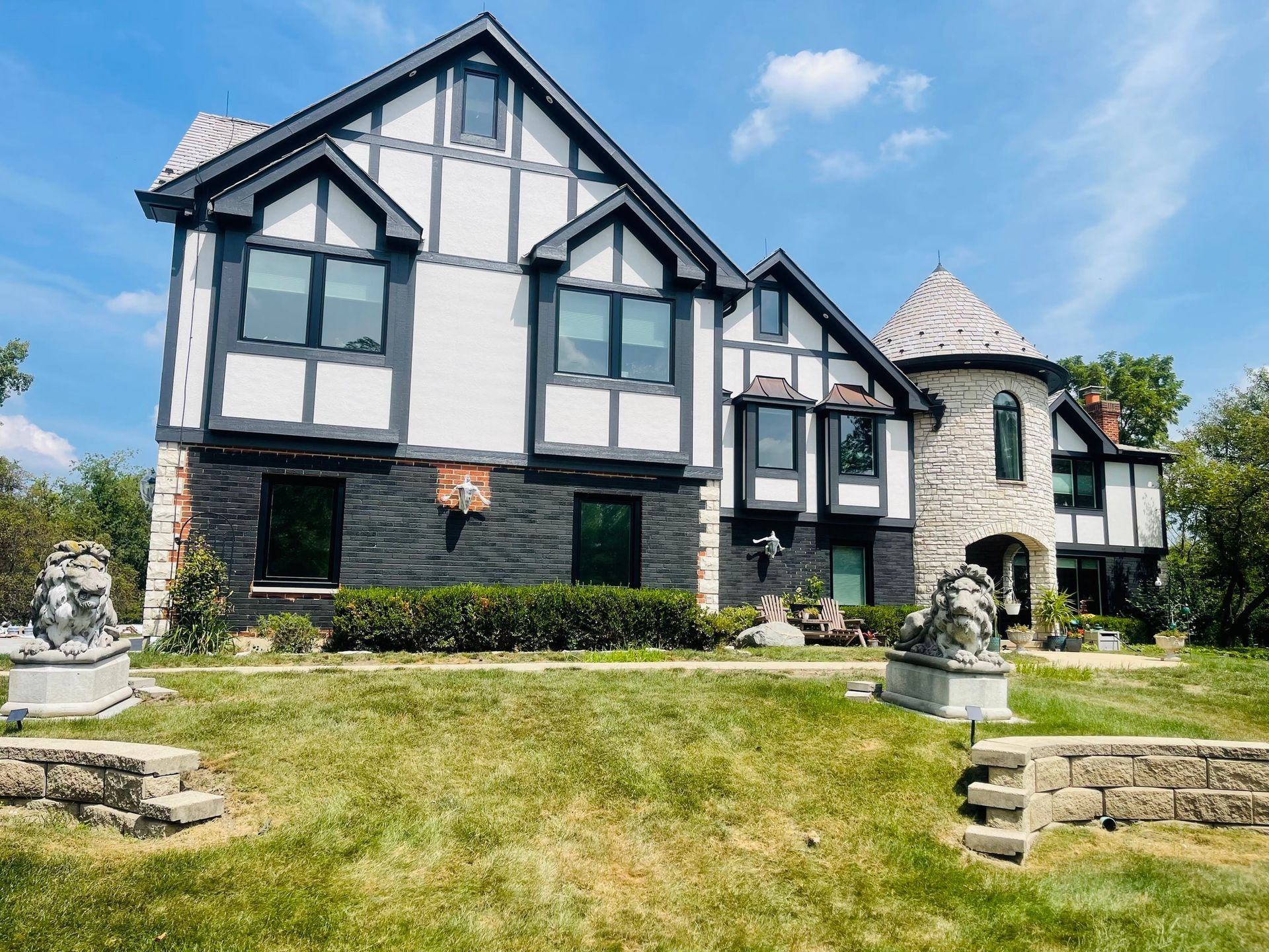Tudor-style house with black and white exterior, stone turret, and lion statues on the lawn.