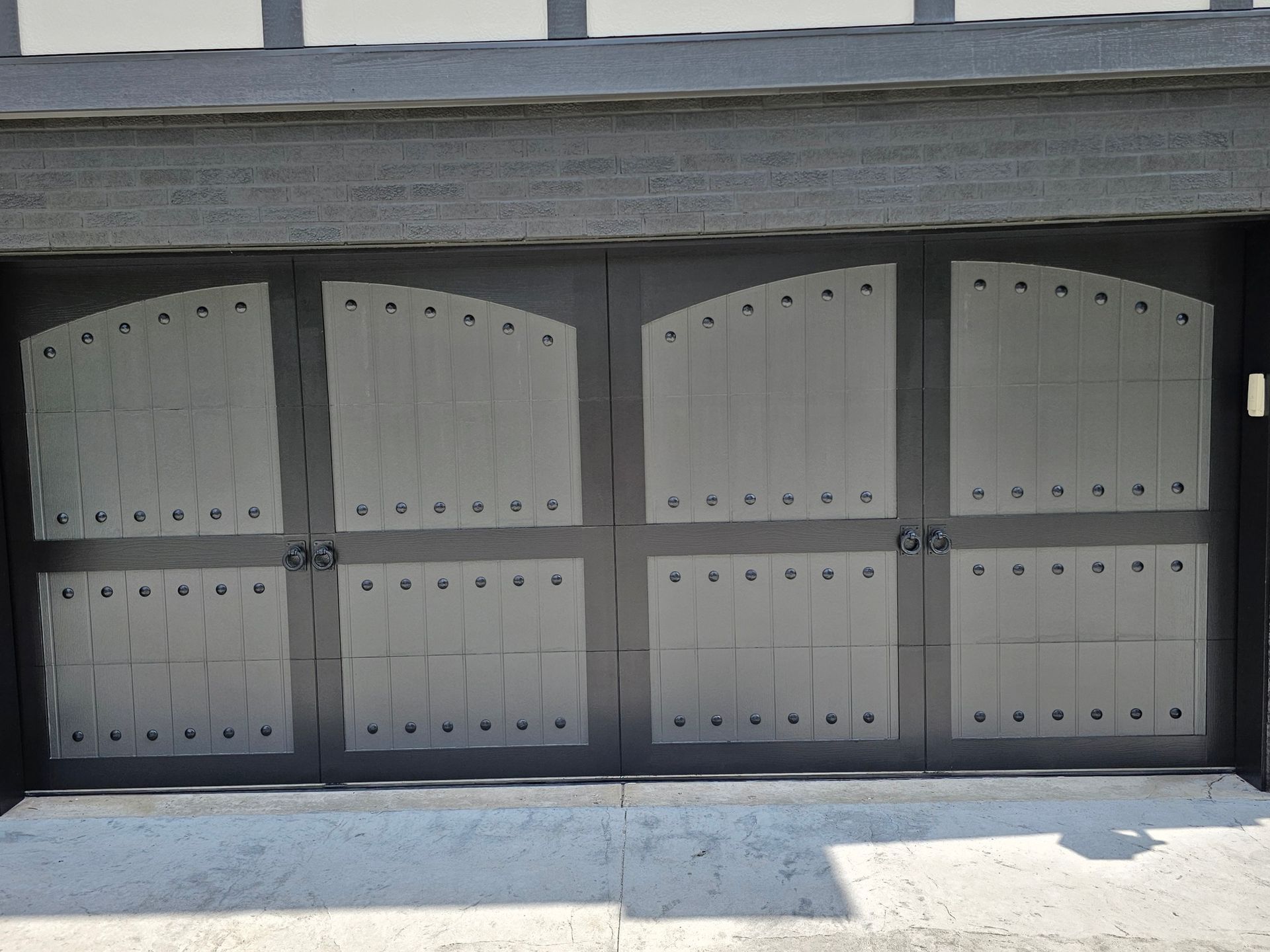 Gray and black garage door with arched top and decorative hardware.