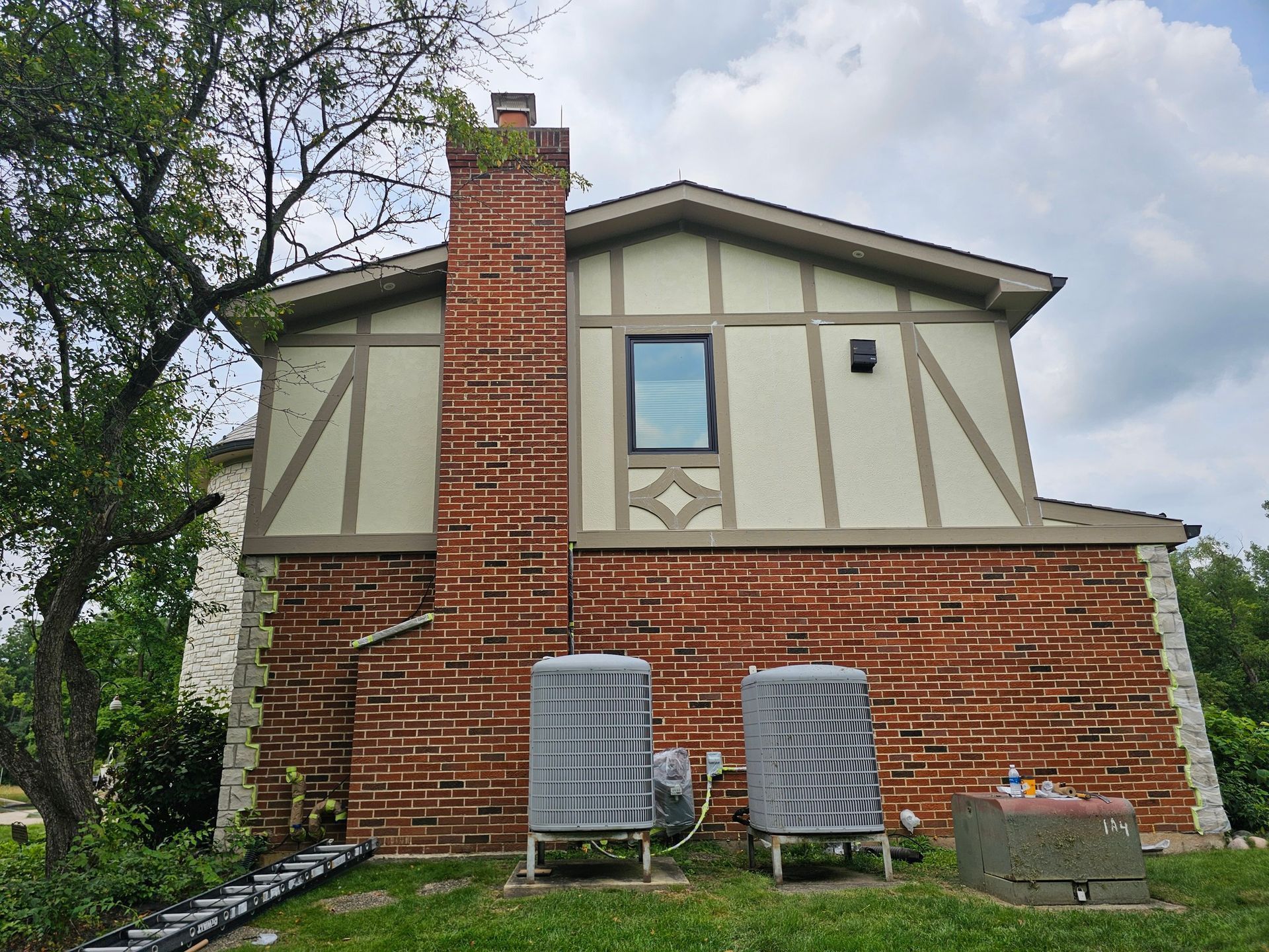 Brick house with chimney; beige and brown accents. Two water tanks on the ground. Cloudy sky.
