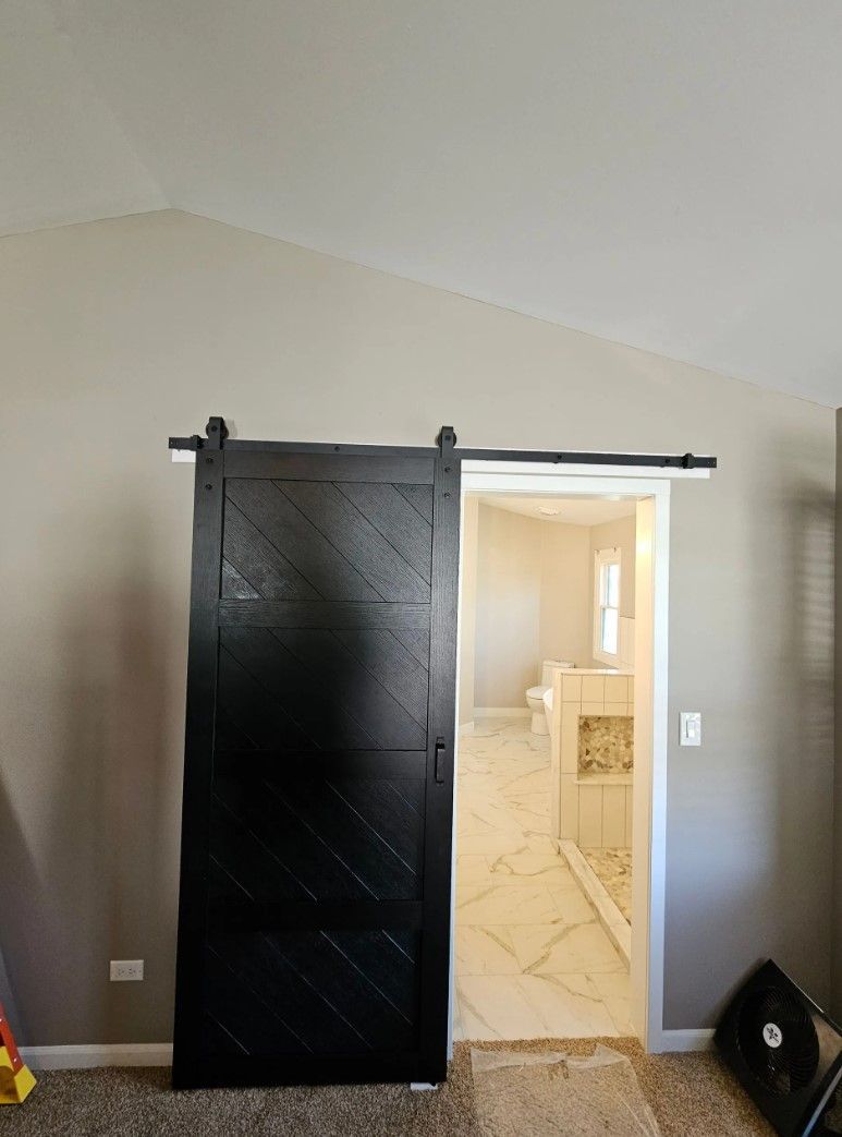 Black barn door partially covering a bathroom entrance, on a white track, against gray walls.