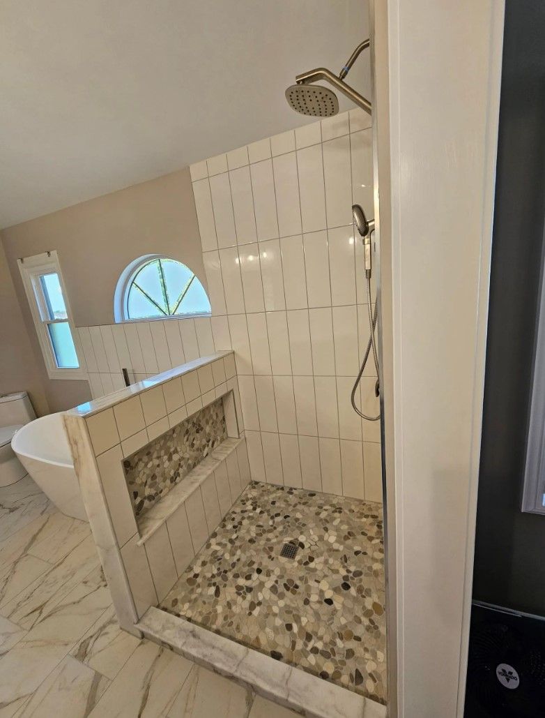 Bathroom with a tiled shower, pebble floor, and soaking tub; neutral tones.