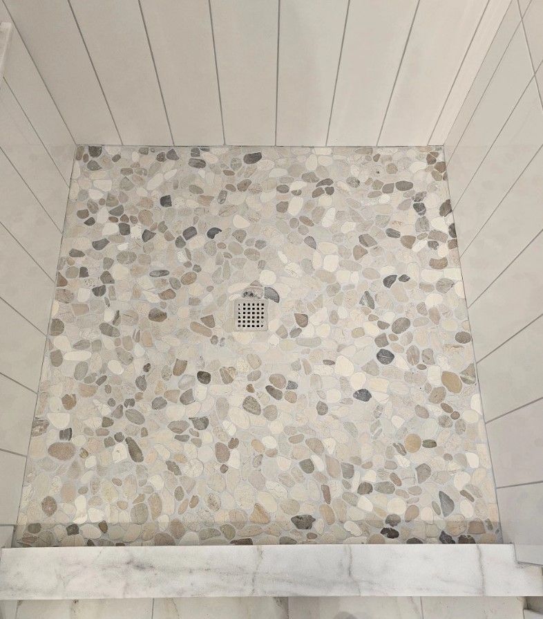 Shower with pebble tile floor, drain, and white plank walls.