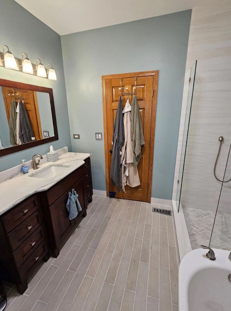Bathroom with a vanity, wooden door with robes, and a bathtub with shower.