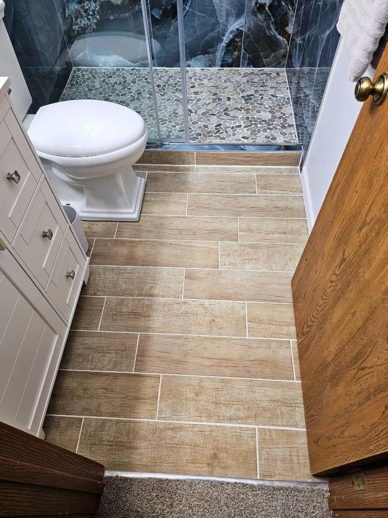 Bathroom with tan tile floor, toilet, vanity, and partially open wooden door.