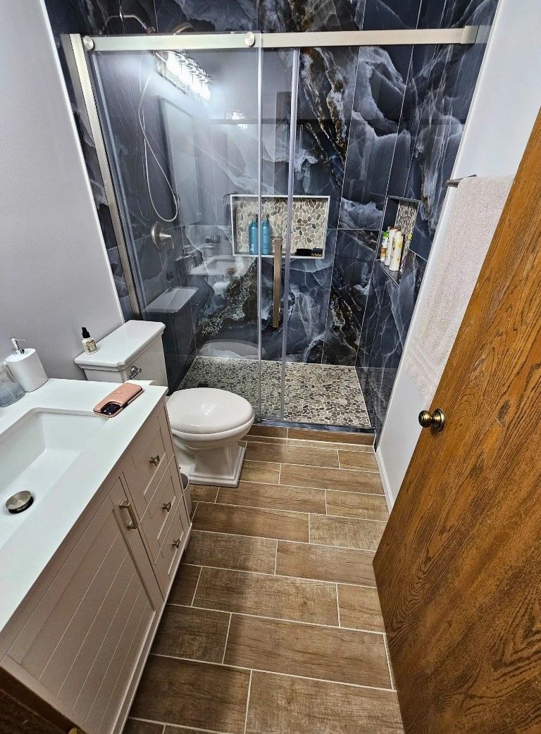 Bathroom with dark blue and white patterned shower, white vanity, and brown flooring.