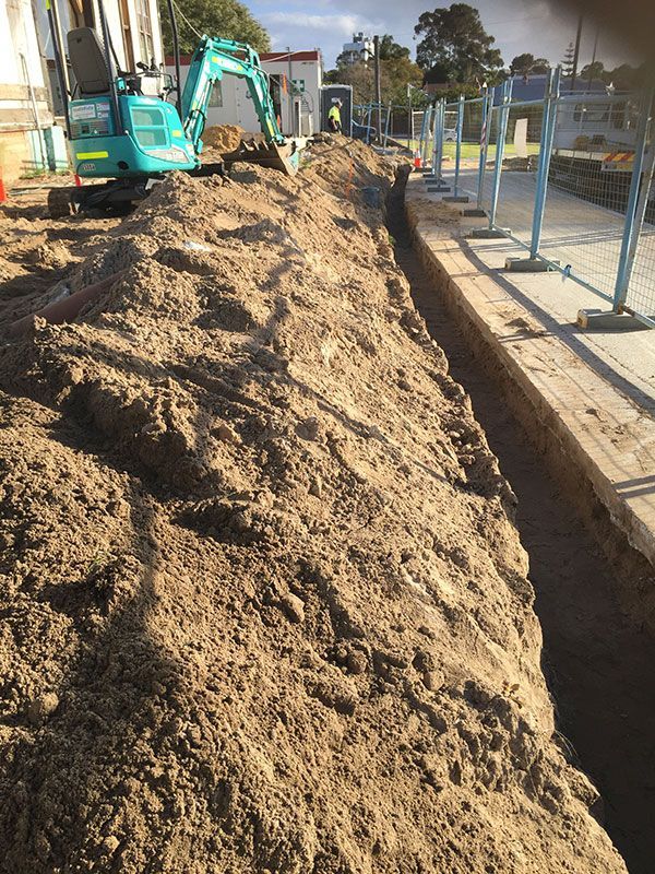 A blue excavator is digging a trench in the dirt