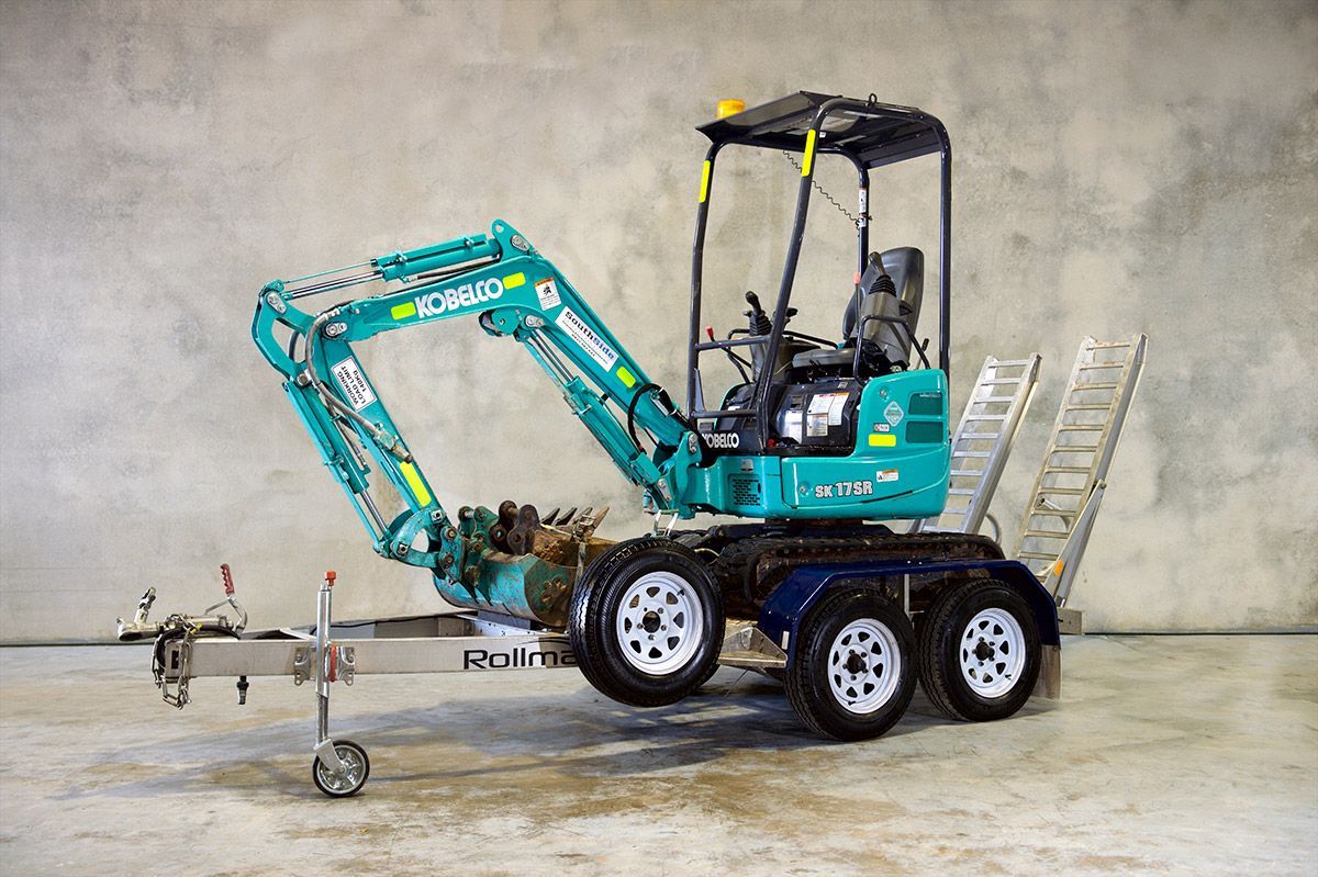 A small excavator is parked on a trailer with a ladder attached to it.