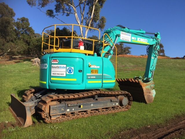 A kobelco excavator is parked in a grassy field