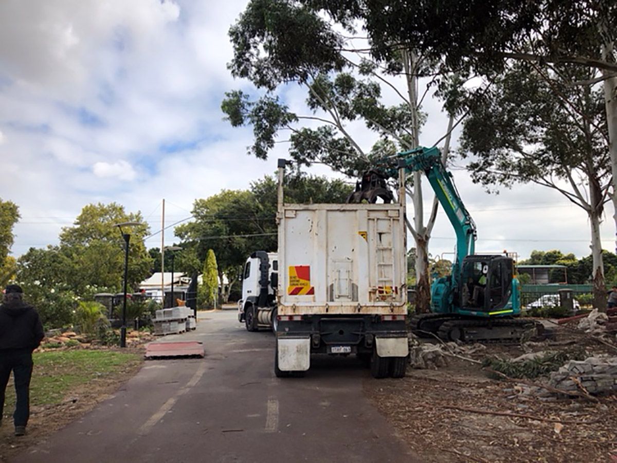 A dump truck is parked on the side of the road next to an excavator.