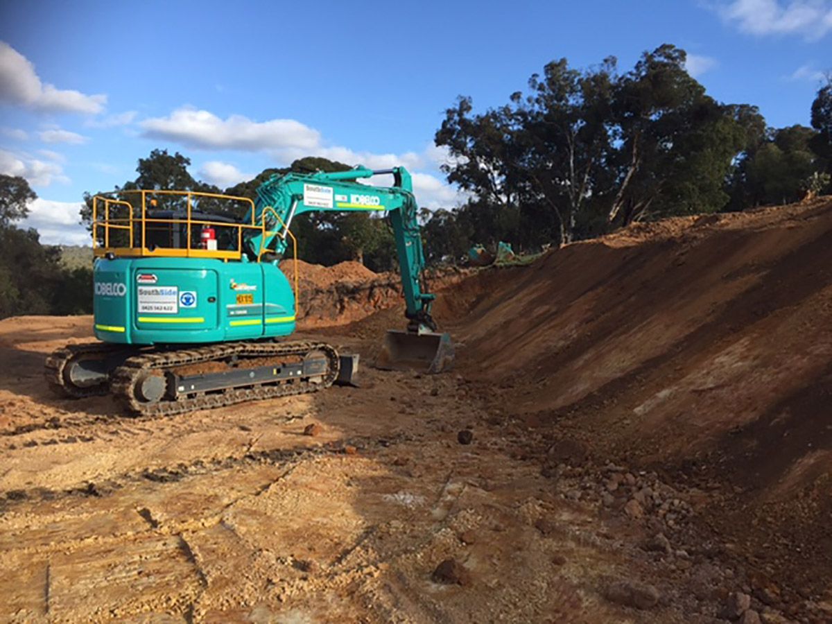 A blue excavator is sitting on top of a dirt hill.